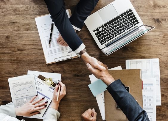 Business people shaking hands over a table with papers and laptops.