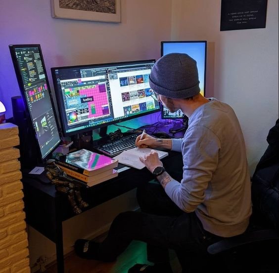 A man sitting at a desk with two monitors, focused on his work,he create a website.