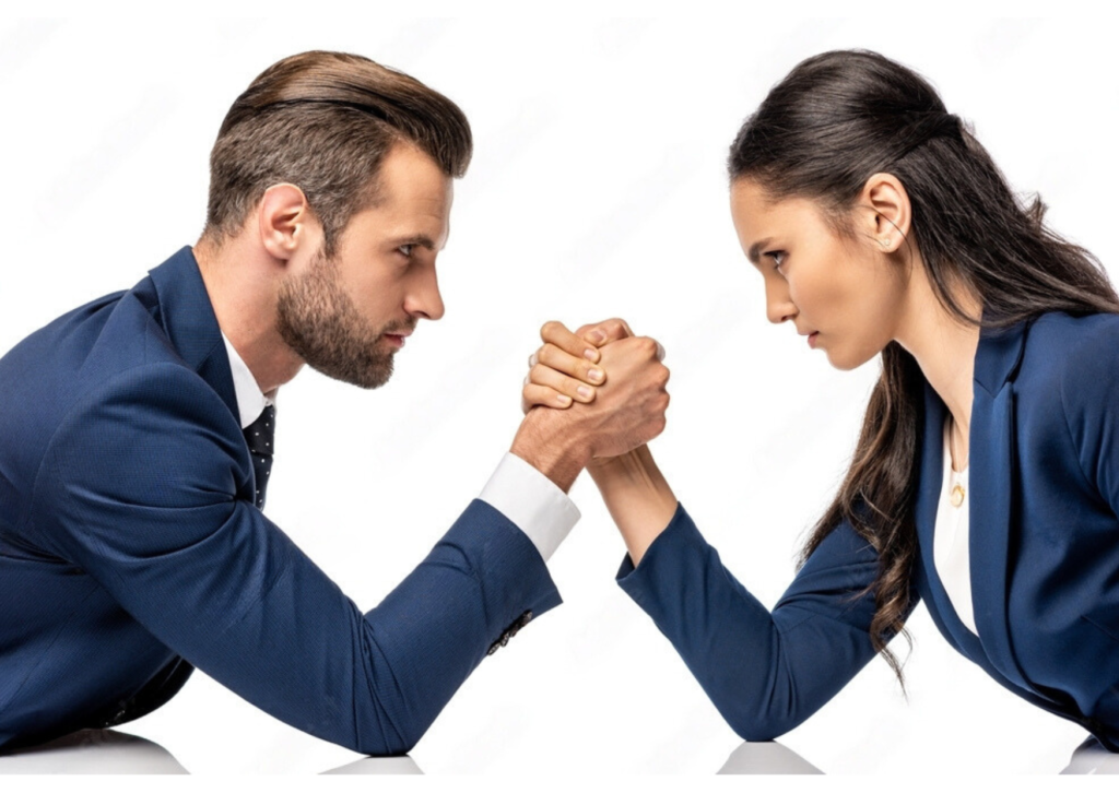 Two business professionals in suits arm wrestling at a conference table.
