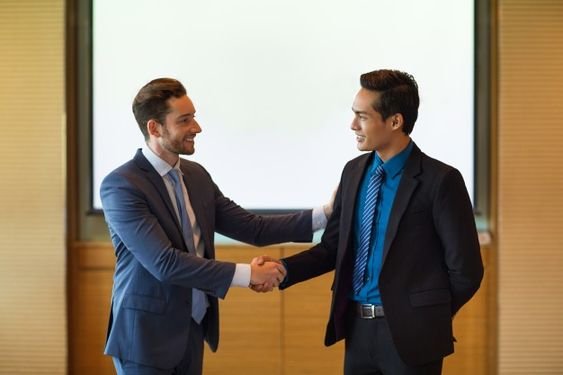 Two businessmen shaking hands in front of a screen, symbolizing progress from startup to success.